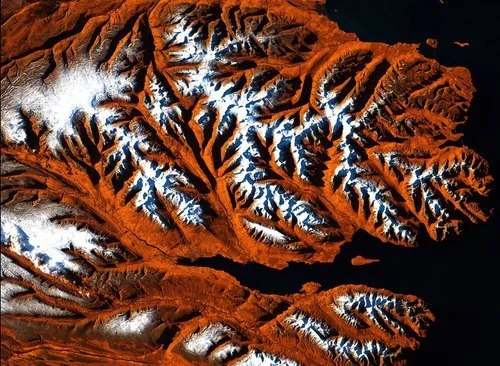Satellite-style image of snow-covered mountains surrounded by reddish terrain.