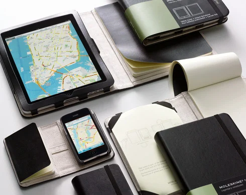 Moleskine-style cases holding a tablet and phone beside paper notebooks.