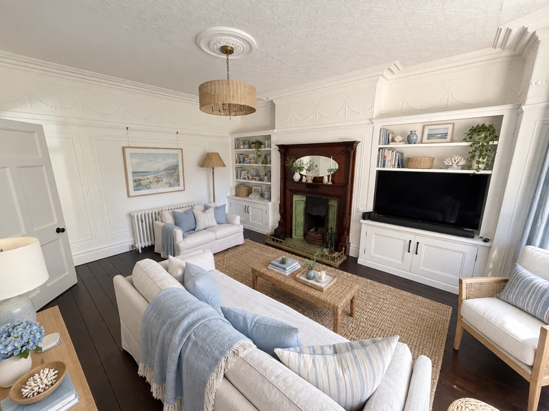 AI-generated coastal redesign with white seating, pale blue cushions, a woven coffee table and pendant, and the original wooden fireplace