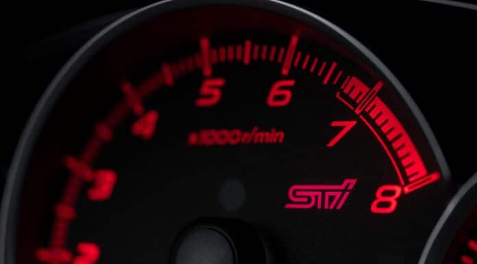 A motor car speedometer, lit in red at night.