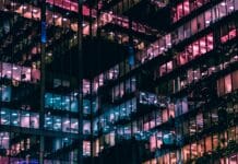 ChatGPT Industry Trends Prompt: Create an Industry Briefing in Minutes City office block windows at night with different colored lighting inside reflecting out off opposing glass walls to create an almost abstract geometric lattice of different colored lights.